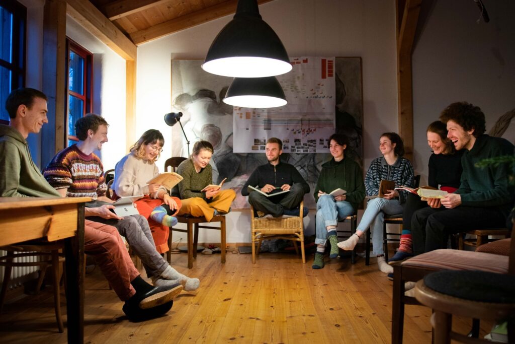 Eine Gruppe junger Menschen sitzt gut gelaunt in einem Stuhlkreis und liest gemeinsam einen Text.